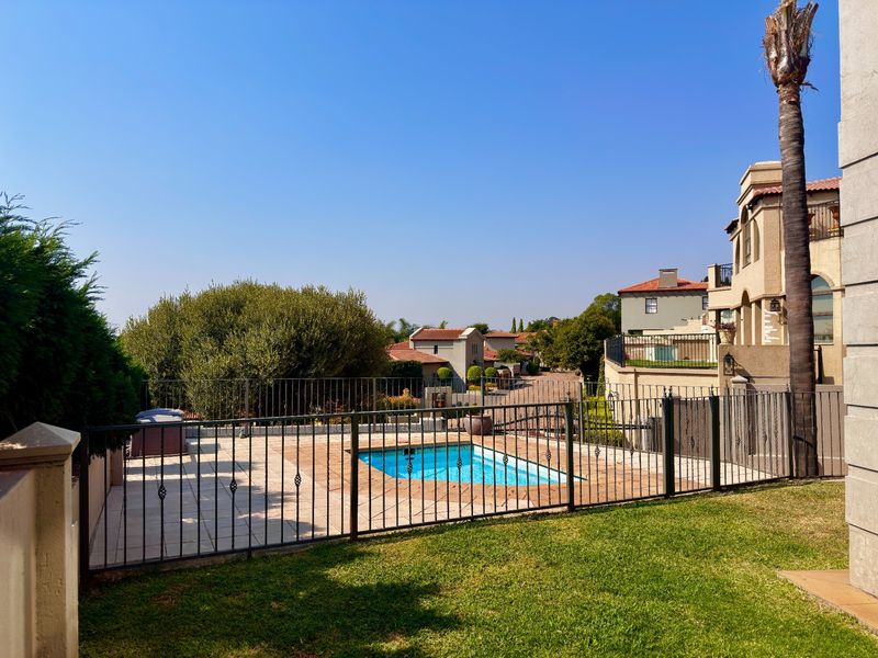 A well-maintained outdoor pool area featuring a paved deck, secure wrought iron fencing, and a manicured lawn in a residential estate setting.