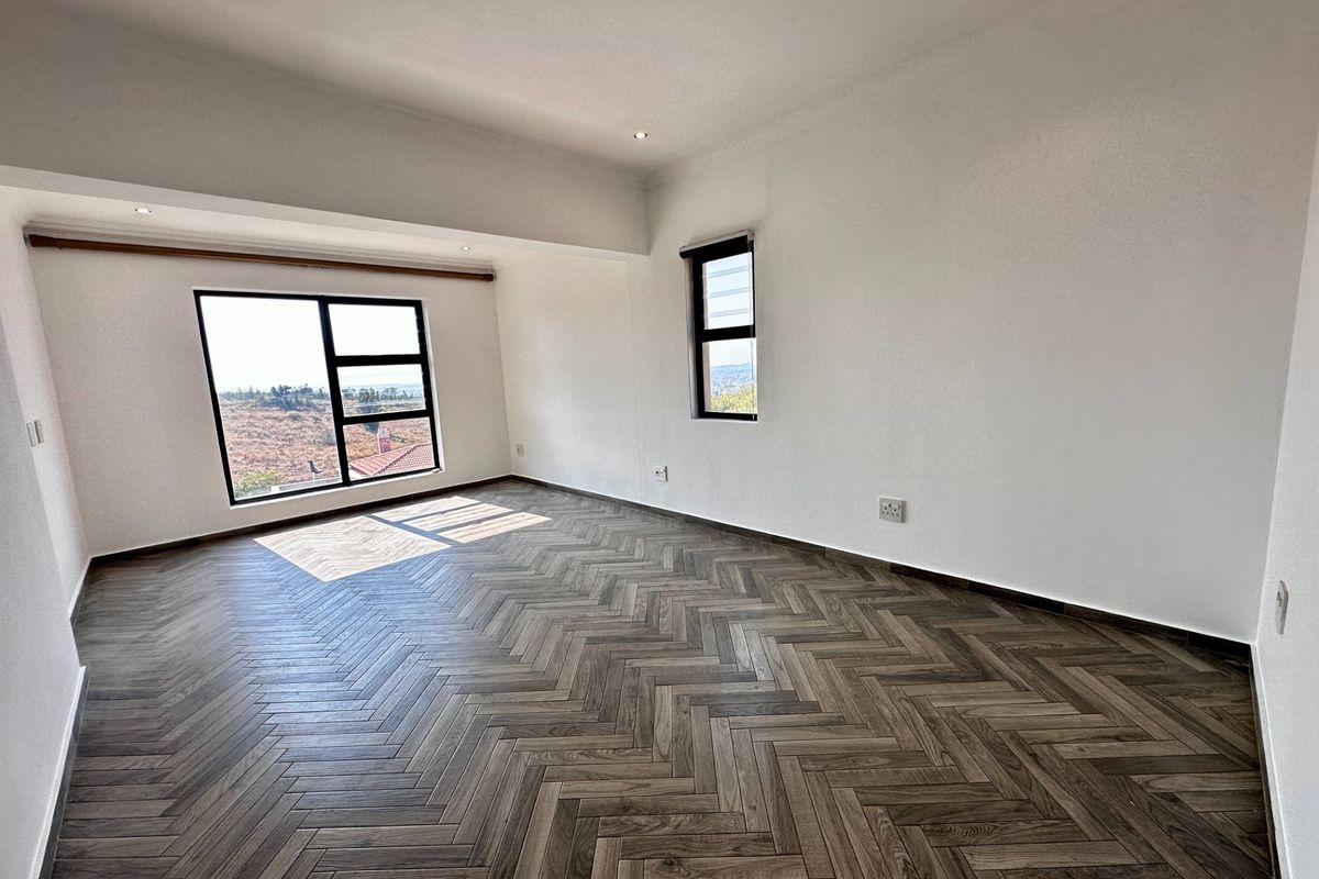 A bright, vacant bedroom featuring modern herringbone wood flooring, recessed downlighting, and large windows with scenic views.