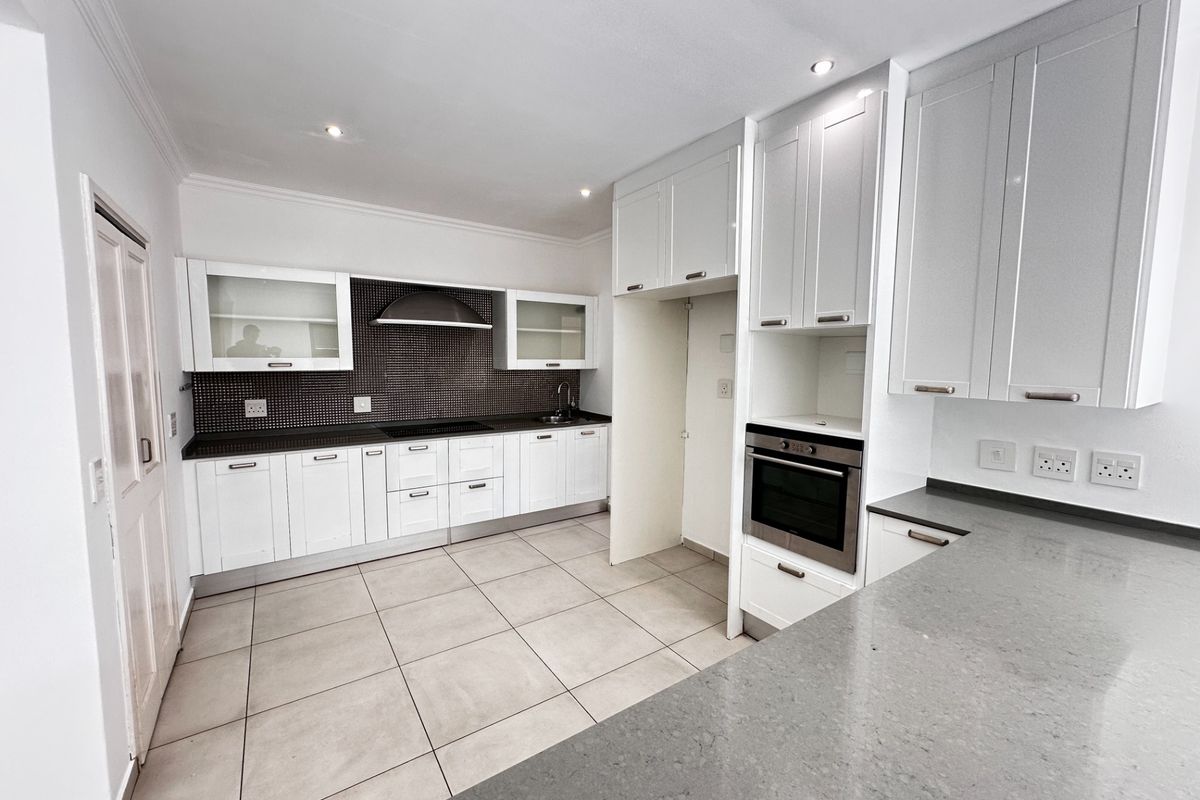 Modern kitchen featuring white cabinetry, stone countertops, integrated oven, electric hob, extractor fan, and tiled flooring in a clean, well-maintained space.