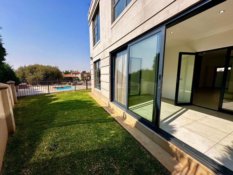 Rear view of the property featuring a tiled patio area with large sliding glass doors, a well-maintained lawn, and a swimming pool.