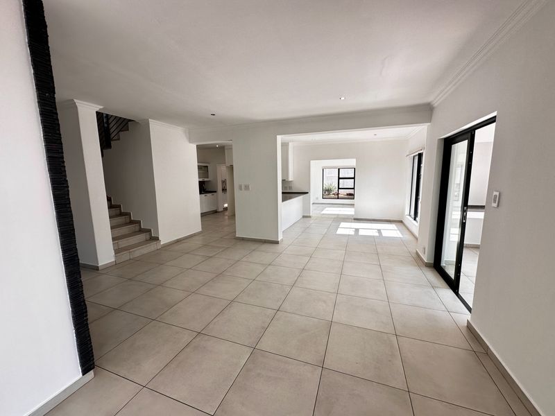 Spacious open-plan living area featuring neutral tiled flooring, recessed lighting, and a staircase, with seamless flow to the kitchen and outdoor access.