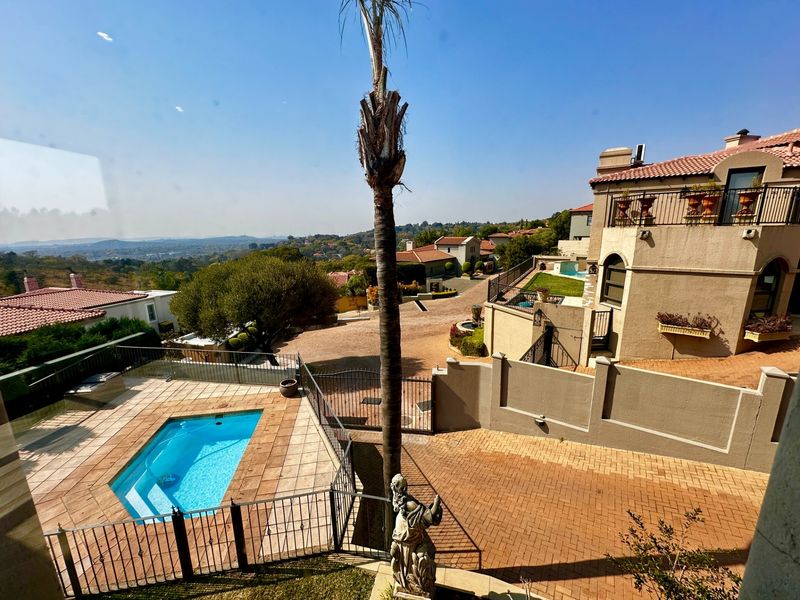Elevated view overlooking a private swimming pool, paved driveway, and surrounding residential estate landscape with clear horizon views.