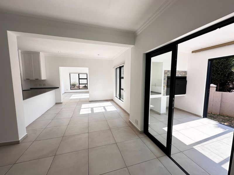 Spacious open-plan living area featuring tiled floors, modern kitchen cabinetry, and seamless access to an outdoor patio with a built-in braai.