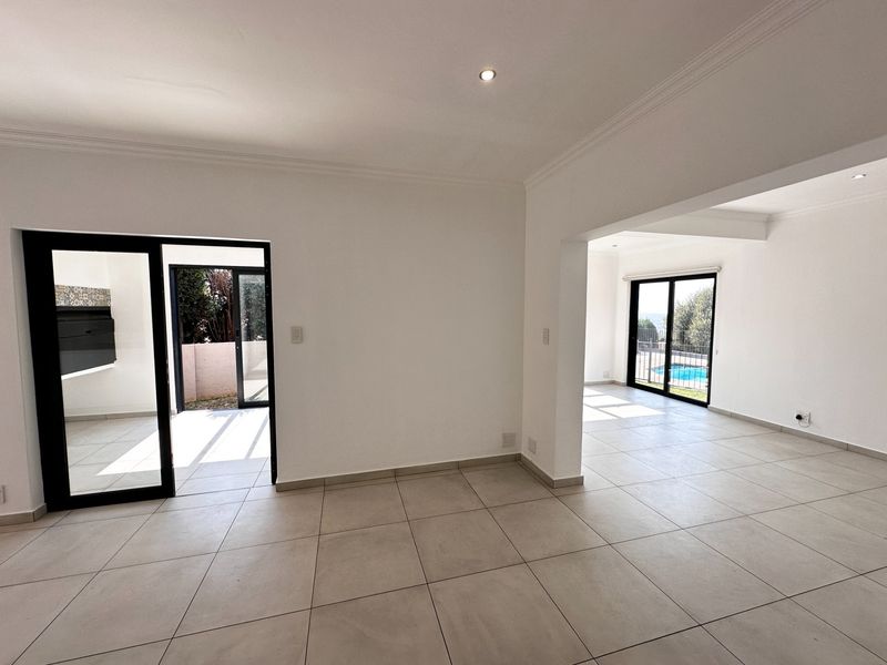 Spacious open-plan living area featuring neutral tiled flooring, recessed lighting, and large sliding glass doors providing access to the outdoor patio and pool area.