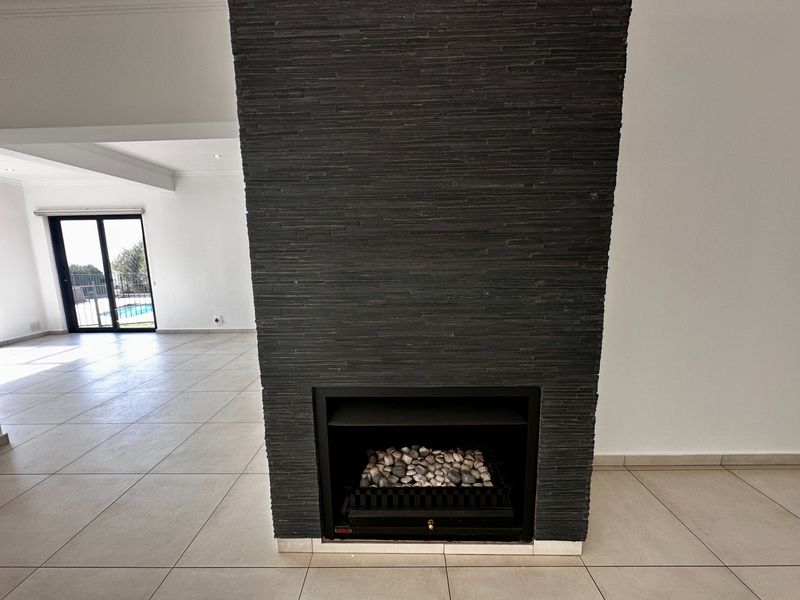 Spacious living area featuring a modern black stone-clad built-in fireplace and neutral tiled flooring, with direct access to the outdoor pool area.