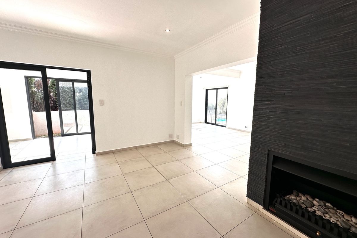 Spacious open-plan living area featuring large format floor tiles, a modern black stone-clad built-in fireplace, and sliding glass doors leading to the outdoor space.