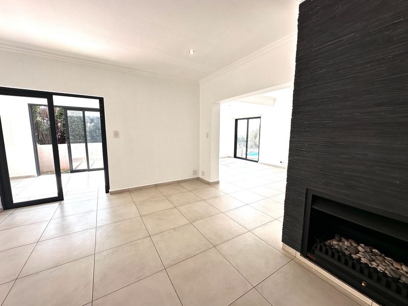 Spacious open-plan living area featuring large format floor tiles, a modern black stone-clad built-in fireplace, and sliding glass doors leading to the outdoor space.
