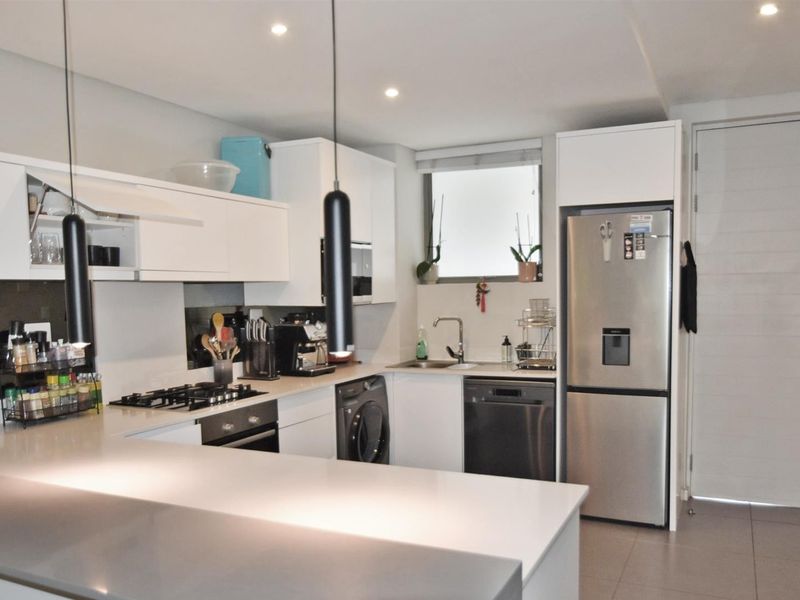Modern kitchen featuring white cabinetry, stone countertops, integrated appliances, gas hob, and recessed lighting in a clean, functional layout.