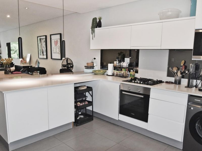 Modern open-plan kitchen featuring sleek white cabinetry, stone countertops, integrated appliances, and a gas hob, seamlessly flowing into the living area.