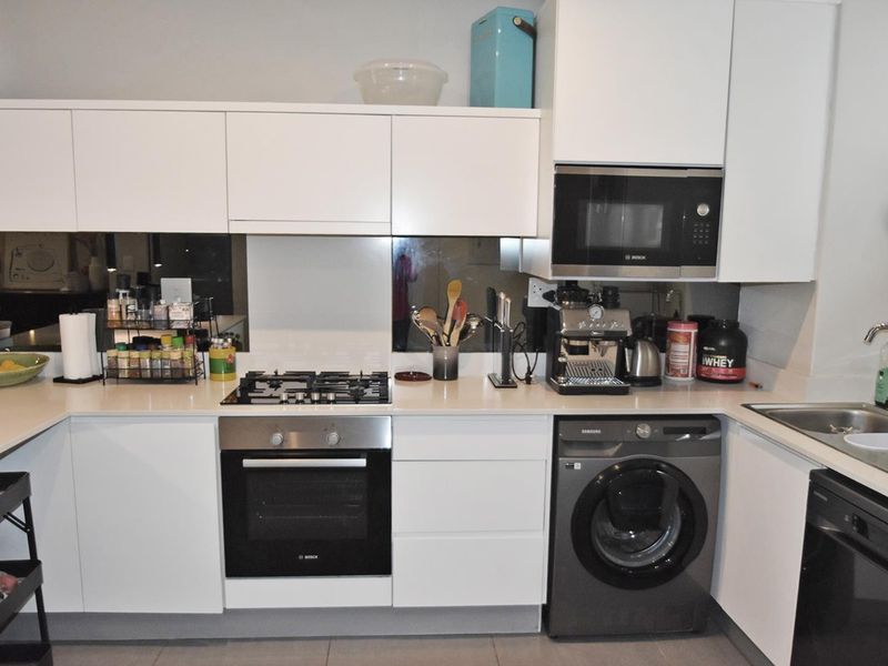 Modern kitchen featuring white cabinetry, gas hob, built-in oven, integrated microwave, and a sleek mirrored splashback with a convenient under-counter washing machine.