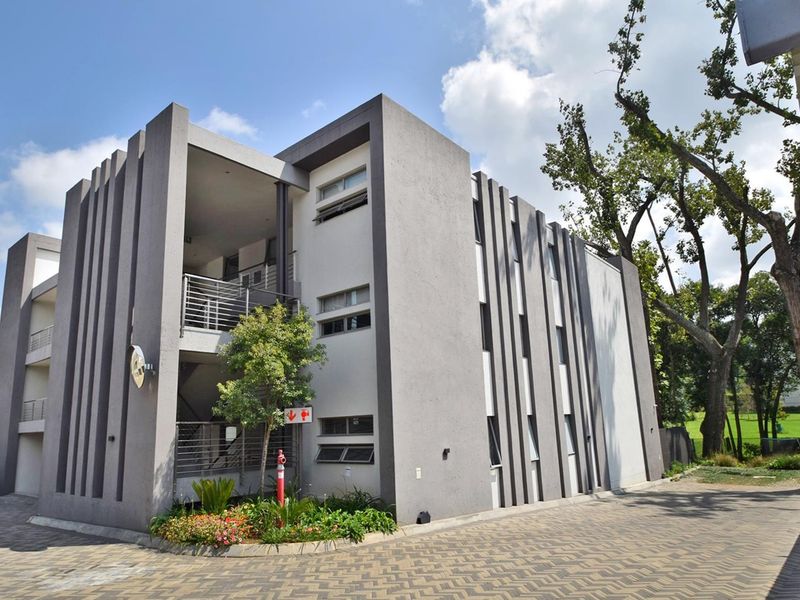 Modern multi-story apartment building exterior featuring contemporary grey facade, paved driveway, and integrated balcony access.