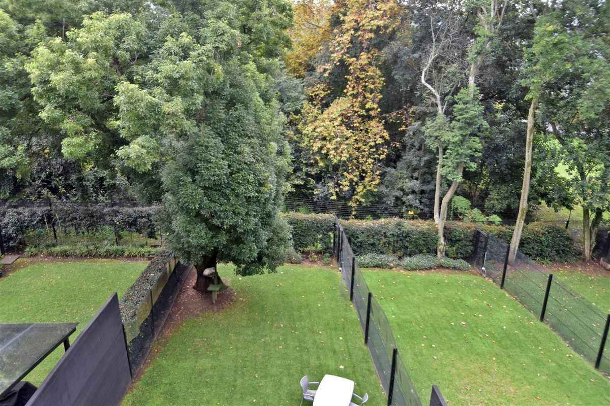 A private rear garden featuring a well-maintained lawn, perimeter fencing, and mature trees providing a leafy, secluded outlook.