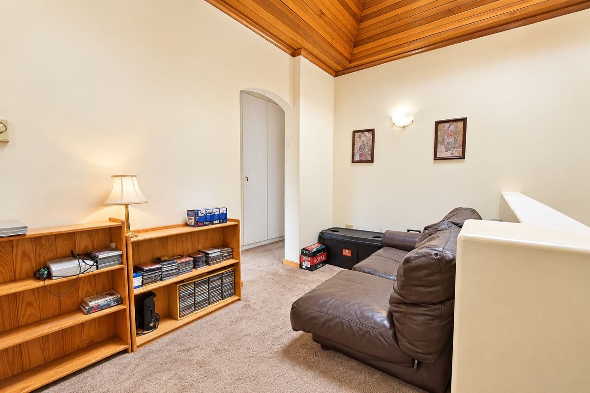 A cozy living area featuring a distinctive timber-clad vaulted ceiling, neutral walls, and an arched doorway leading to a built-in storage cupboard.