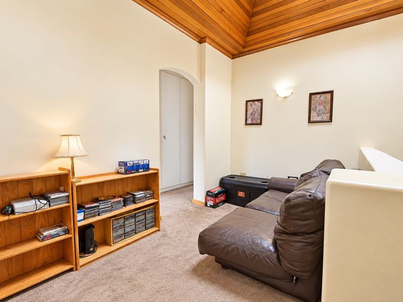 A cozy living area featuring a distinctive timber-clad vaulted ceiling, neutral walls, and an arched doorway leading to a built-in storage cupboard.