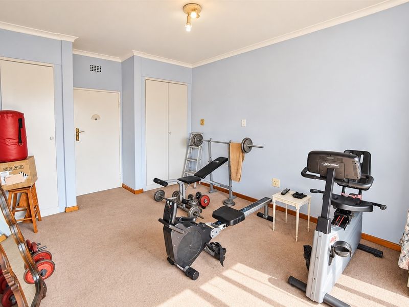 A bedroom currently utilized as a home gym, featuring neutral wall paint, carpeted flooring, and built-in storage cupboards.