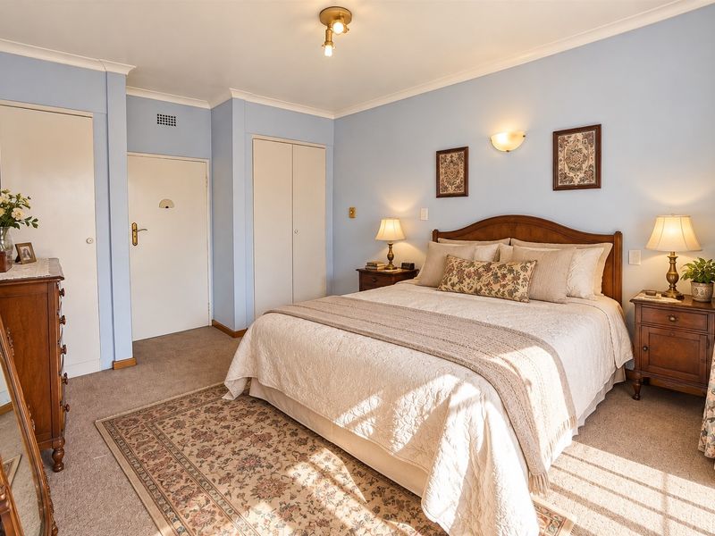 A well-maintained bedroom featuring built-in cupboards, neutral carpeting, and classic wall-mounted lighting, offering a comfortable and functional living space.