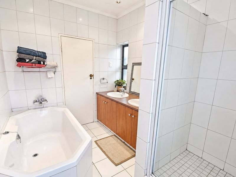 A functional bathroom featuring a built-in vanity with dual basins, a separate bathtub, and a tiled shower enclosure.