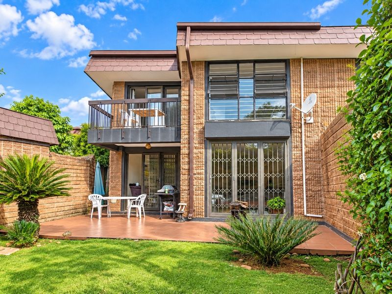 Rear view of the townhouse featuring a paved patio area, a private balcony, and a small enclosed garden with brick boundary walls.