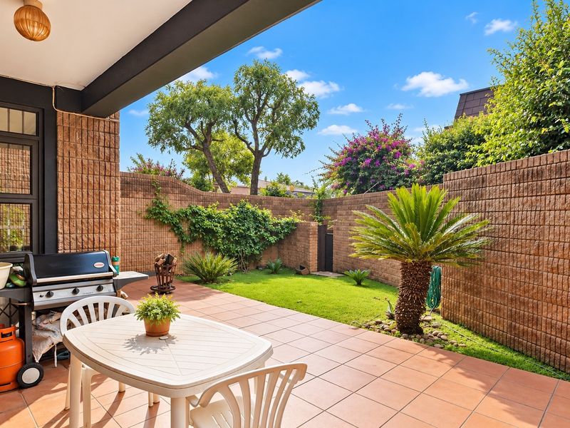 A private covered patio area featuring tiled flooring and a brick boundary wall, overlooking a well-maintained garden space.