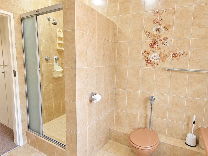 A functional bathroom featuring a shower enclosure, toilet, and neutral tiled finishes throughout, offering a clean and practical space.