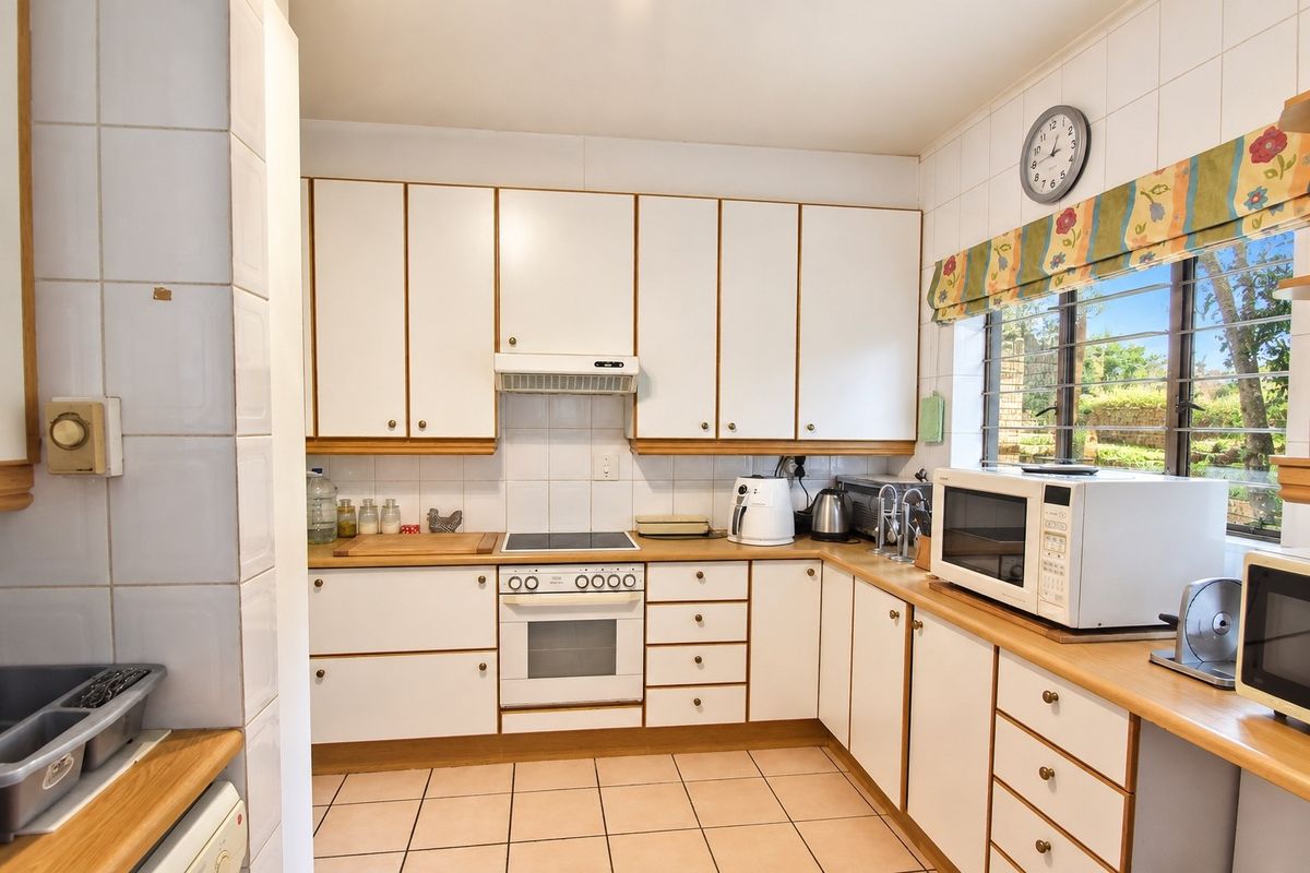 A functional kitchen featuring white cabinetry, built-in oven and hob, tiled splashbacks, and tiled flooring, offering a practical layout with natural light.