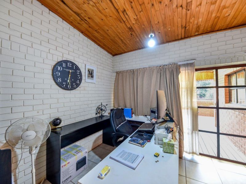 A functional home office featuring exposed brick walls, a warm timber ceiling, and direct access to an outdoor area through a glass panel door.