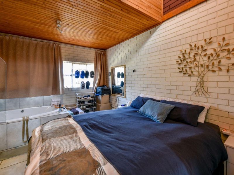 Bedroom featuring exposed brick walls, a timber ceiling, and an integrated bathtub, offering a unique layout with tiled flooring.