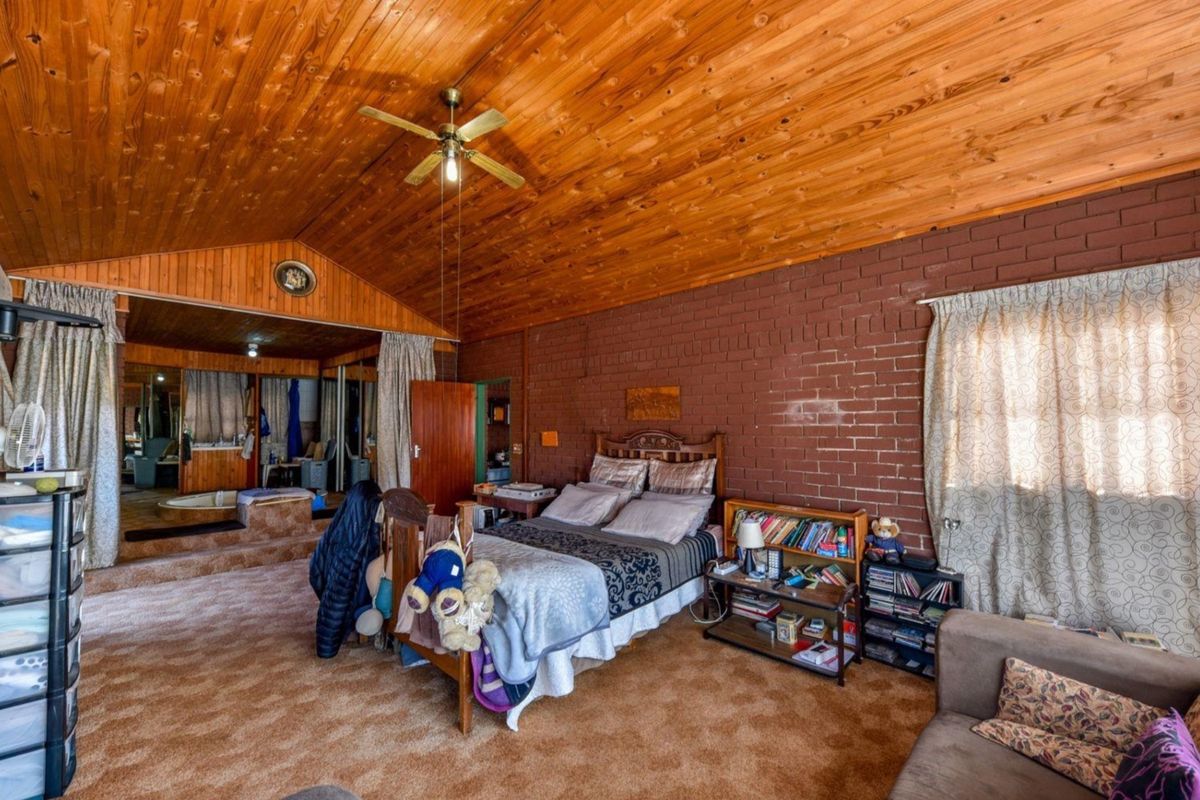 Spacious bedroom featuring an exposed timber vaulted ceiling, brick feature wall, and a raised platform area with built-in storage.