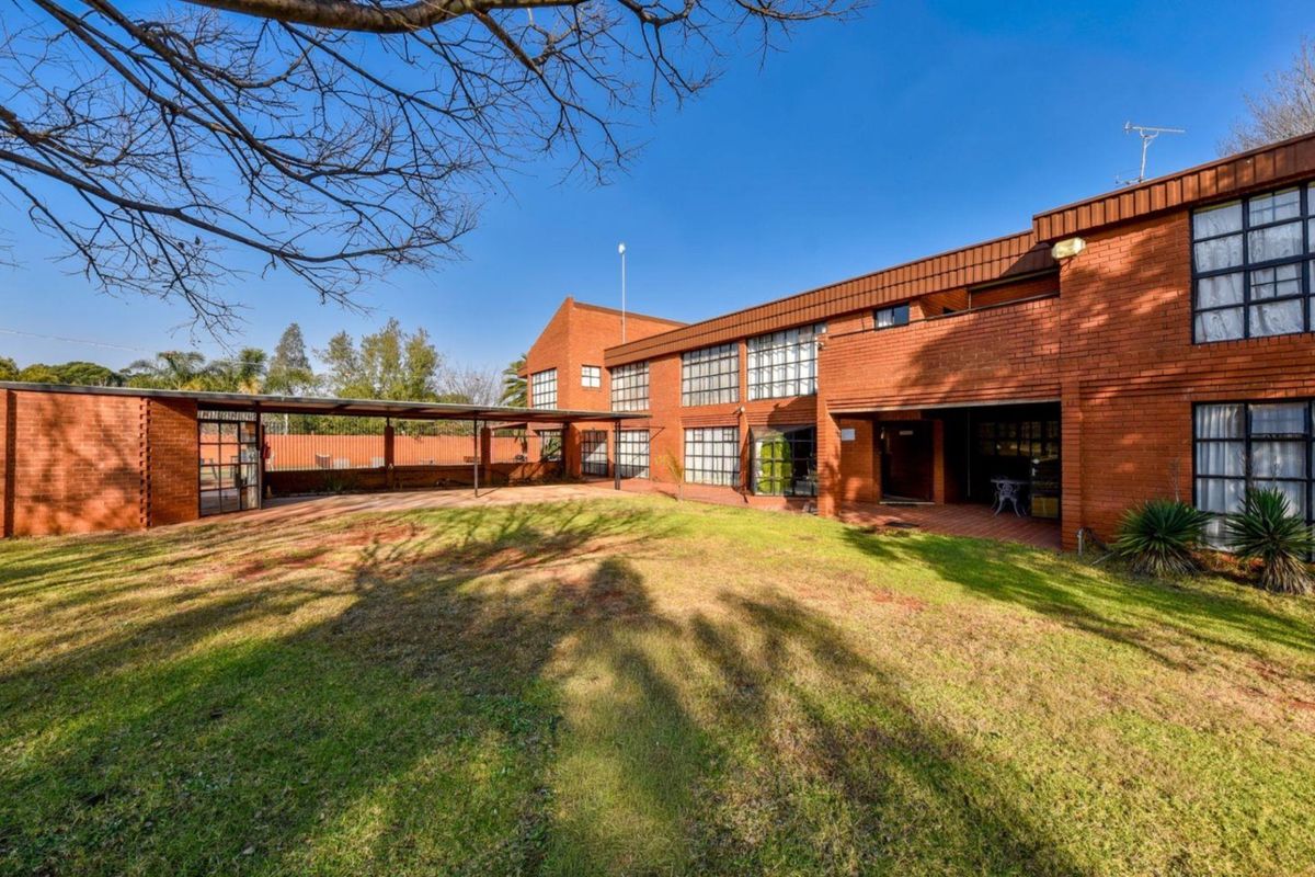 Rear view of a multi-story brick farmhouse featuring a large lawn, covered patio area, and expansive windows.