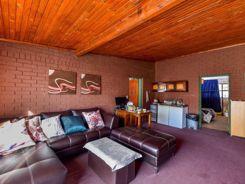 Open plan living area featuring exposed timber ceilings and brick walls, including a small kitchenette area with built-in cabinetry and sink.