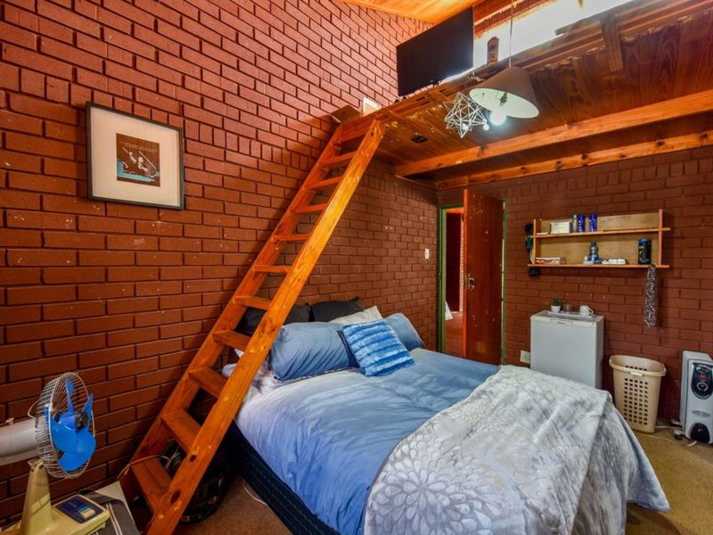 A rustic bedroom featuring exposed brick walls, a timber loft ladder leading to an upper level, and a timber-paneled ceiling.