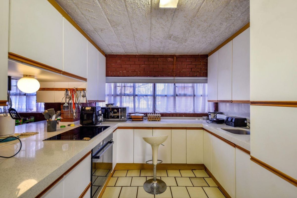 A functional U-shaped kitchen featuring white cabinetry, stone countertops, an integrated electric hob and oven, and a distinctive exposed brick feature wall.