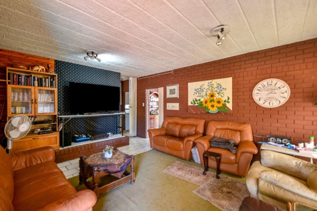 A living room featuring exposed brick walls, tiled flooring, and a built-in brick hearth, offering a rustic aesthetic with potential for modernization.