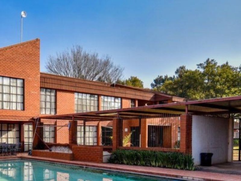 Exterior view of a farm property featuring a swimming pool, covered patio area, and traditional red brick architecture with steel-framed windows.