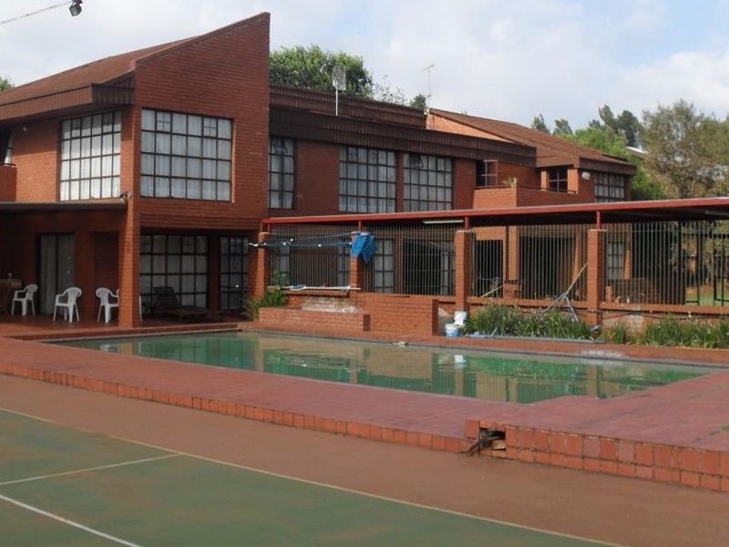 Spacious outdoor entertainment area featuring a swimming pool, brick paving, and a tennis court, set against a large multi-story brick farmhouse.