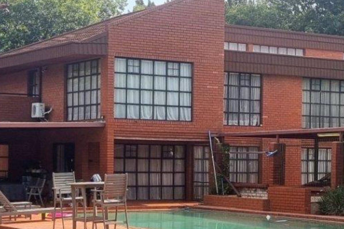 Rear view of a multi-story brick farmhouse featuring a swimming pool, patio area, and large multi-pane windows.