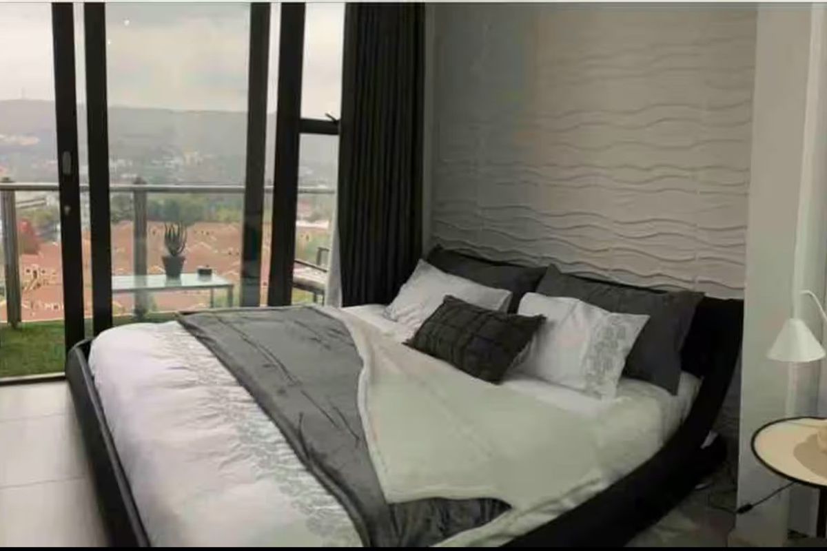 Modern bedroom featuring a textured feature wall, tiled flooring, and large sliding glass doors opening onto a private balcony with scenic views.