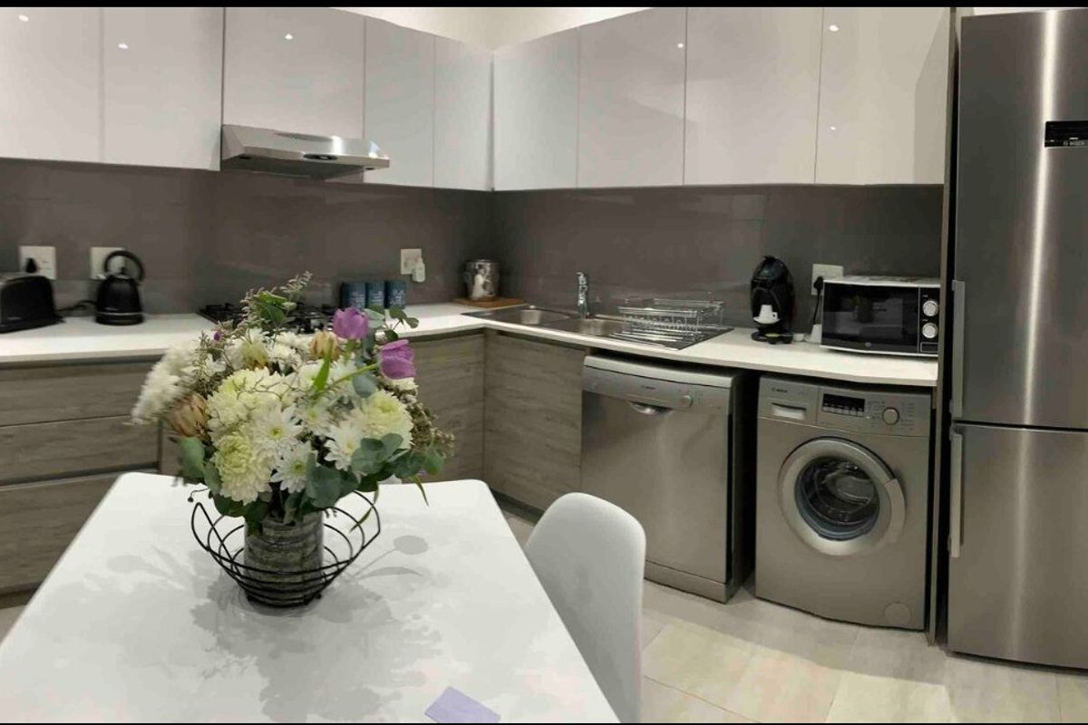 Modern kitchen featuring sleek white and wood-grain cabinetry, stone countertops, integrated appliances, and a functional layout with a gas hob and extractor fan.