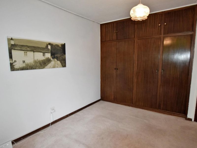 A bedroom featuring built-in wooden wardrobes, neutral carpet flooring, and a central ceiling light fixture.