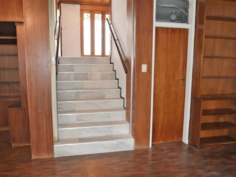 A hallway featuring a tiled staircase with a wooden handrail, flanked by built-in wooden shelving units and parquet flooring.