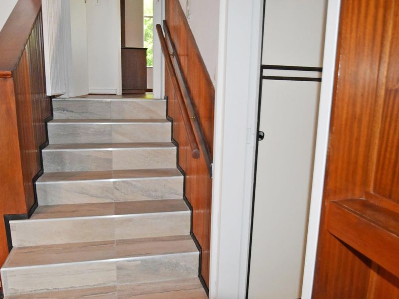 A staircase featuring tiled steps, wooden handrails, and wood-paneled walls, leading to an upper landing with an adjacent built-in storage cupboard.