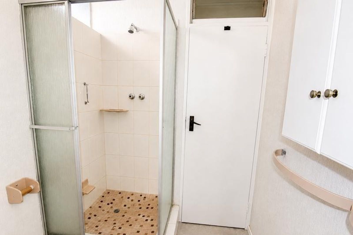 A functional bathroom featuring a corner shower enclosure with tiled flooring and wall-mounted storage cabinetry.