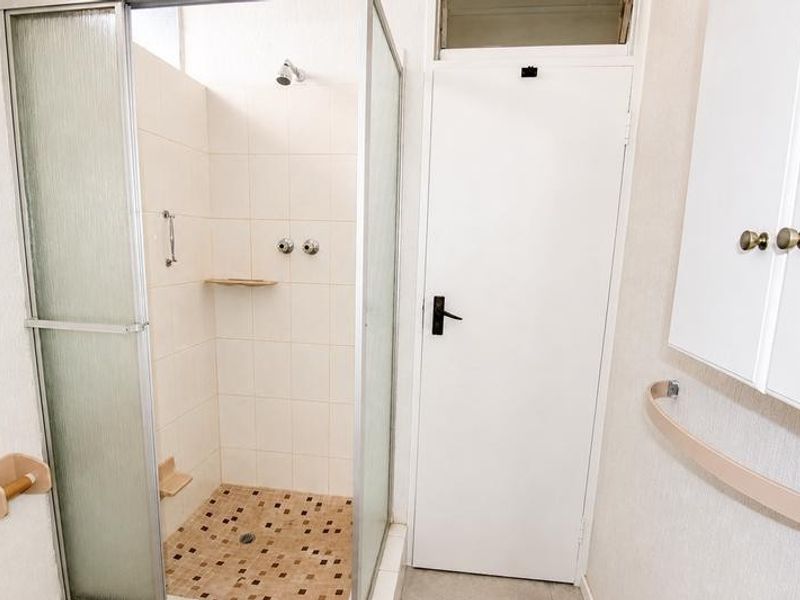 A functional bathroom featuring a corner shower enclosure with tiled flooring and wall-mounted storage cabinetry.
