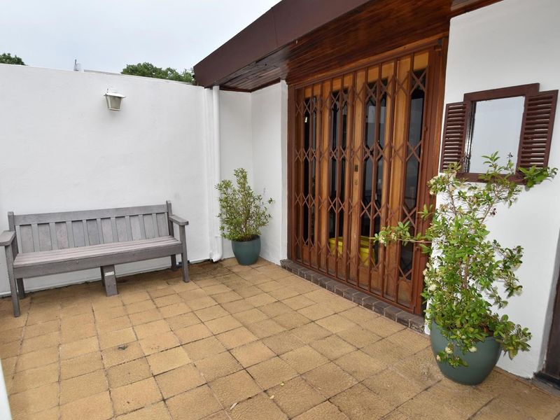 A private paved patio area featuring a secure metal gate entrance, timber door frame, and wall-mounted lighting, offering a functional outdoor space.
