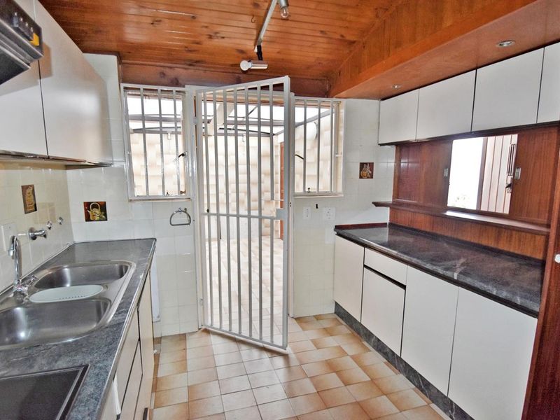 A functional kitchen featuring built-in cabinetry, laminate countertops, a double stainless steel sink, and a security gate leading to an outdoor area.