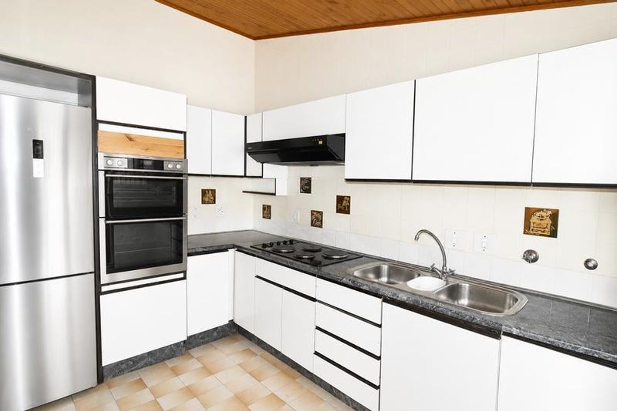 A functional kitchen featuring white cabinetry, built-in double oven, electric hob, and double sink with a tiled backsplash and timber ceiling.