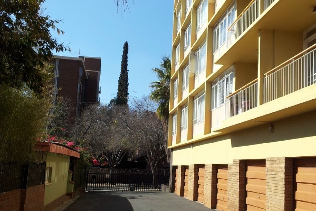 Exterior view of an apartment building featuring a paved driveway, ground-level garage access, and multi-story balconies with metal railings.