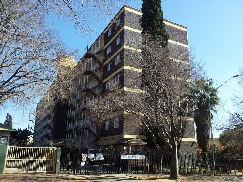 Exterior view of a multi-story apartment building featuring a brick facade, external fire escape staircase, and secure gated entrance.