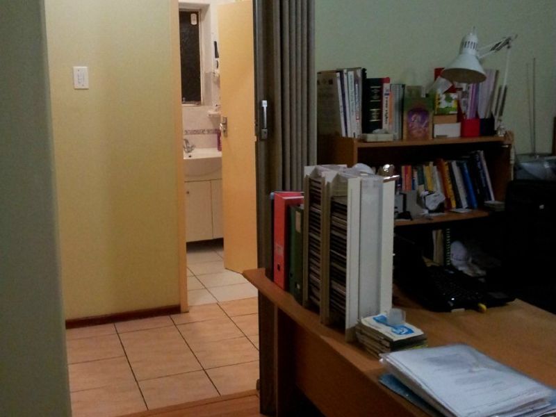A home office space featuring laminate flooring, leading through a sliding door to an adjacent bathroom with a vanity unit.