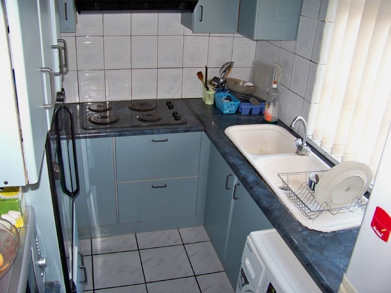 Compact kitchen featuring blue cabinetry, dark laminate countertops, an electric hob, extractor fan, and a double basin sink with tiled backsplash and flooring.